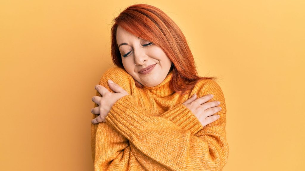 A woman looks cozy in an orange sweater and orange matching room
