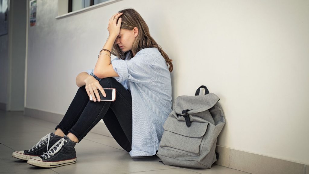 A distressed school age girl sits on a floor