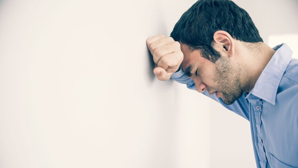 A distressed looking man holds his head against a wall