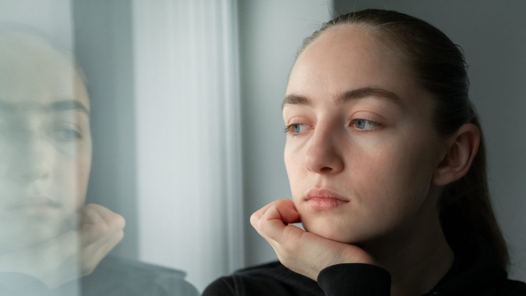 A melancholy looking woman looks out through a window
