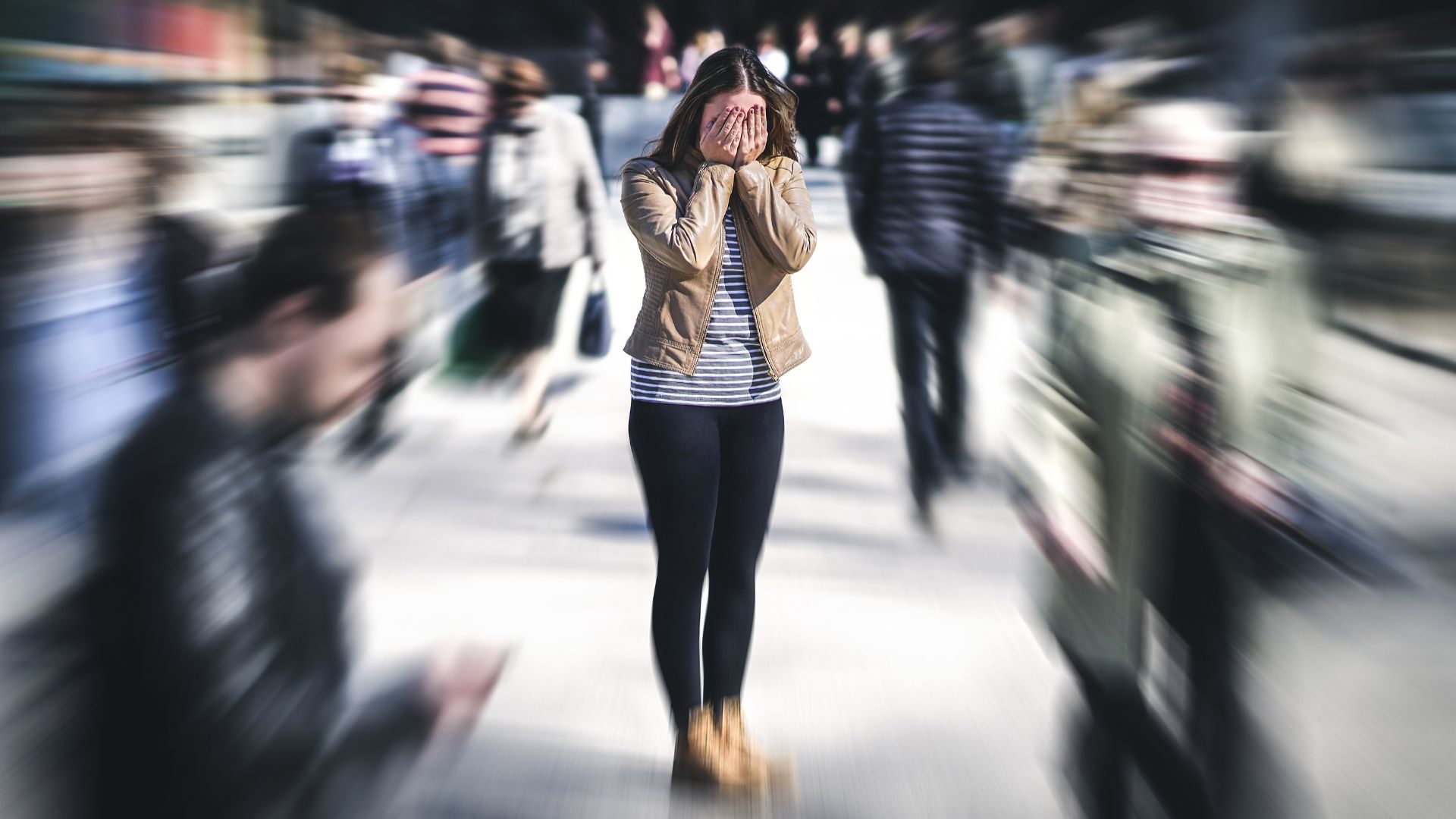 A distressed woman covering her face while a crowd of people around her are edited into a blur