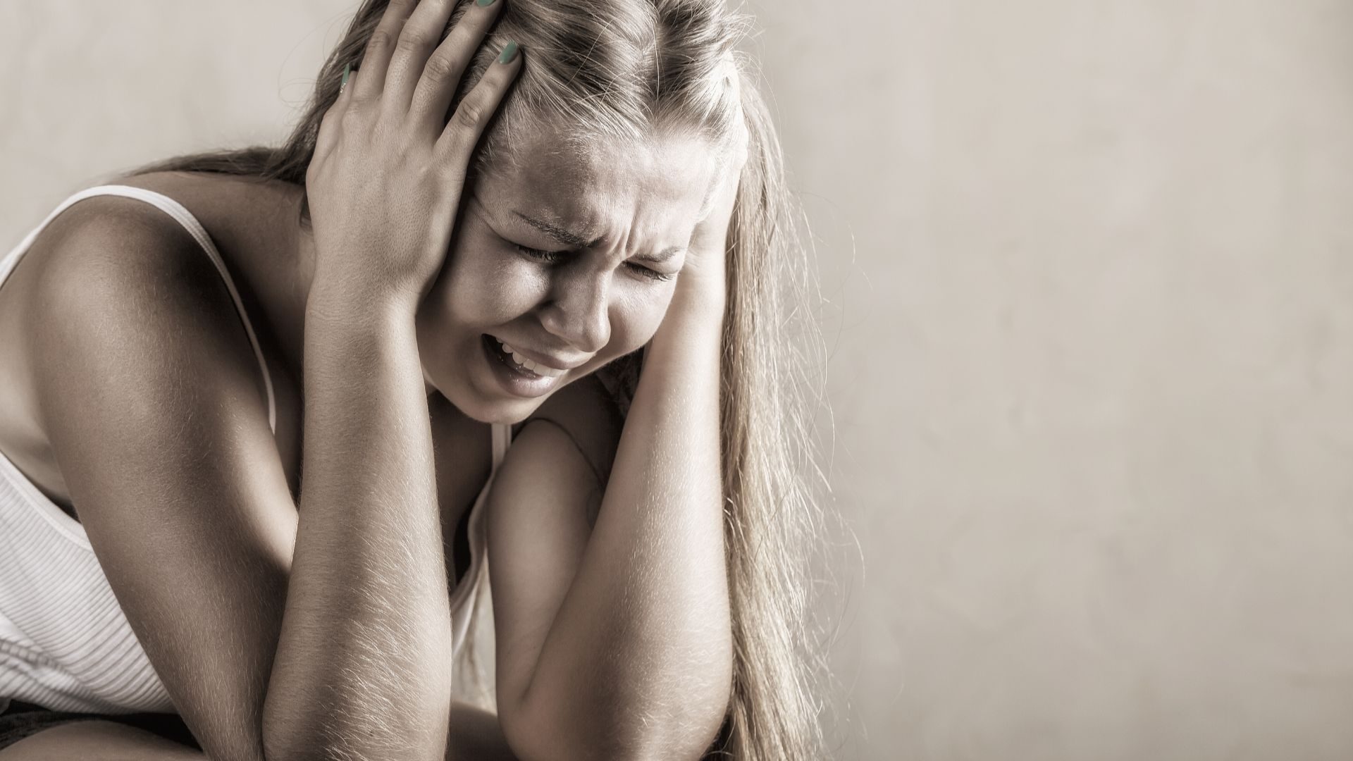 A young woman with hands over her temples closes her eyes and yells