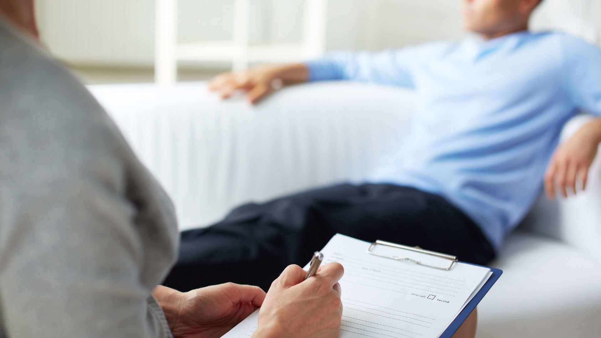 Close up of a therapist's note pad and an out of focus man on a couch