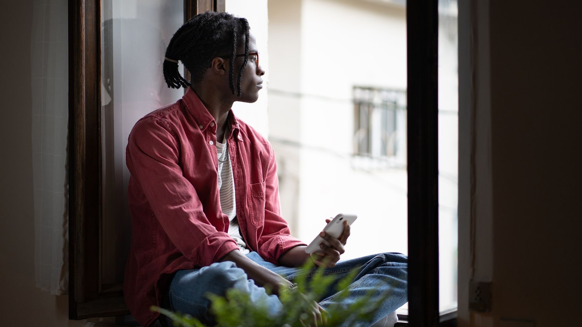 A melancholy man looks out through an open apartment window