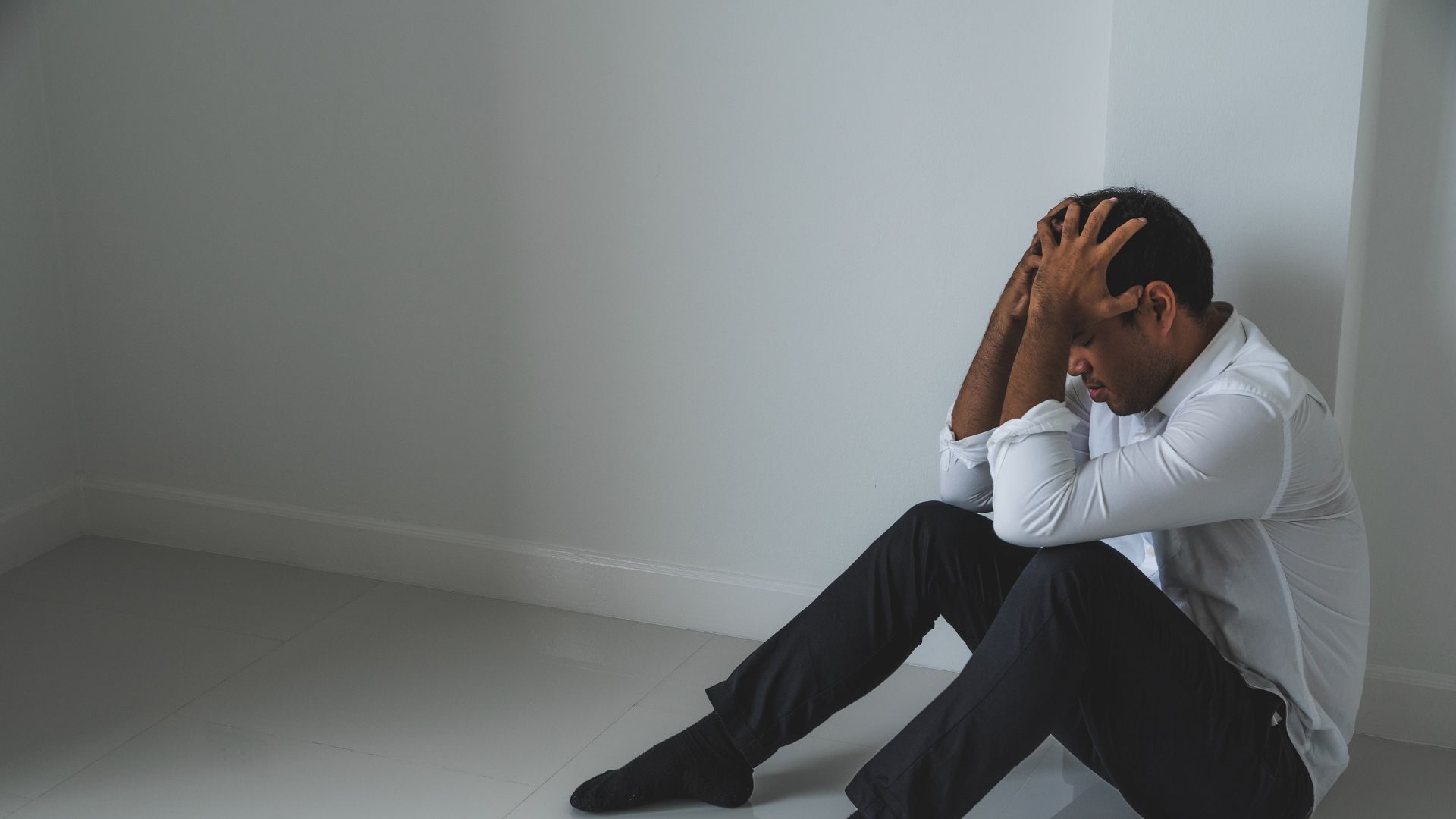 A distressed looking man sitting on the floor in an otherwise cold, empty room