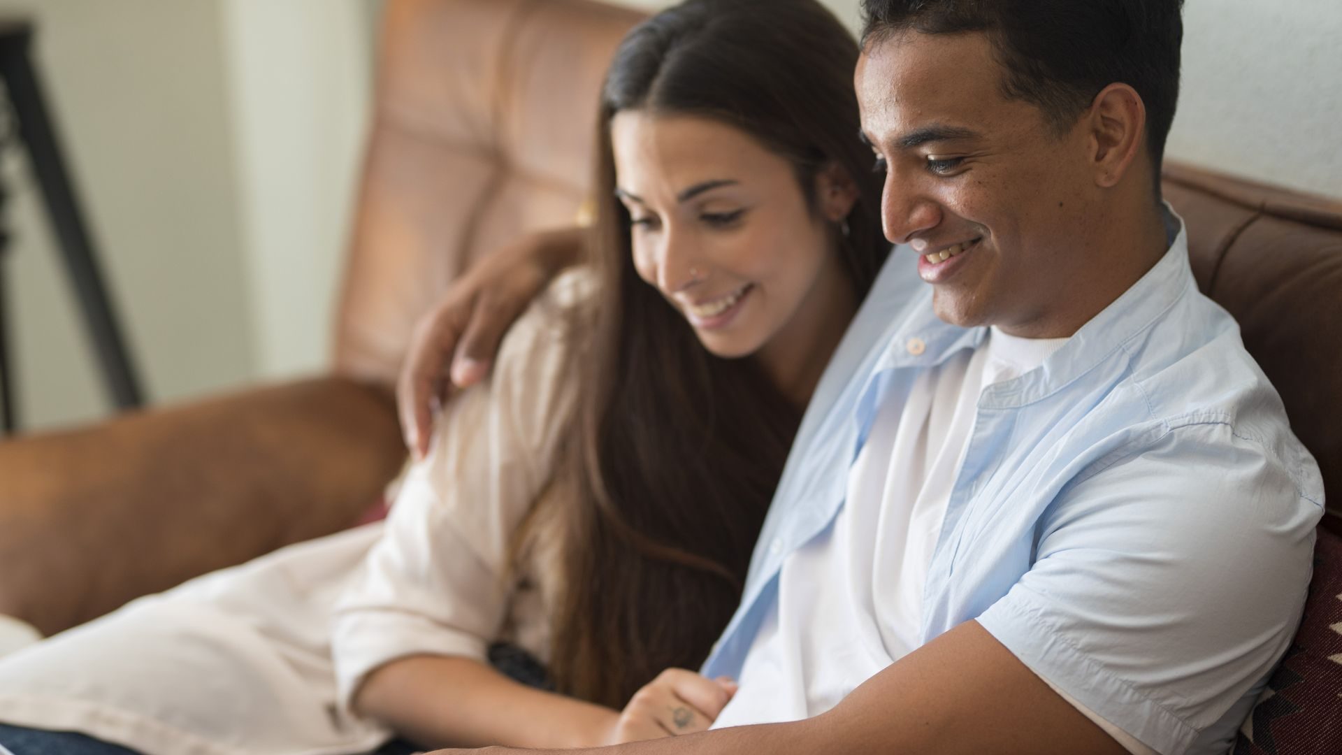 A content looking couple on a couch gaze smiling at something outside the frame of the photograph