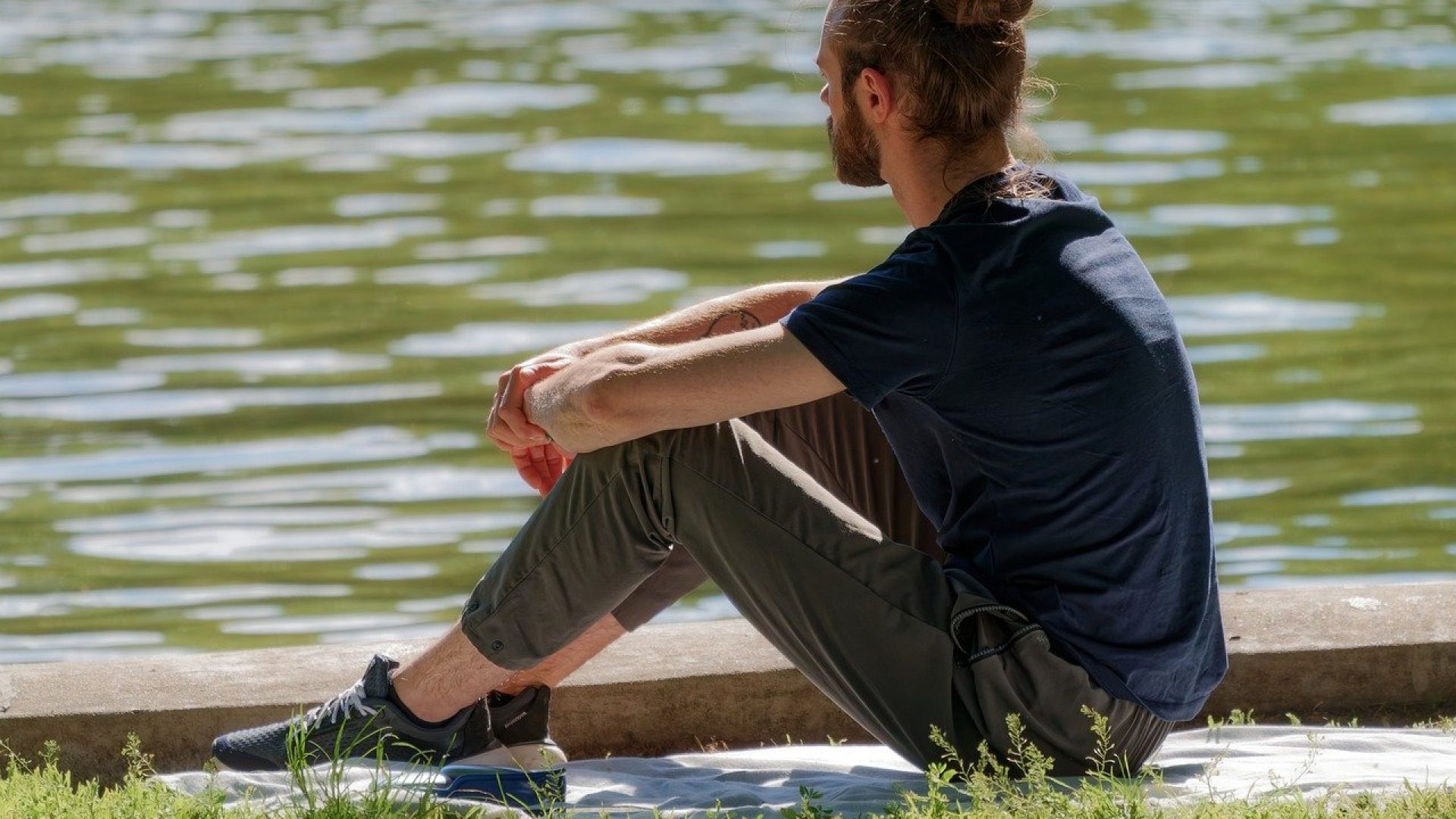 A man with arms on his knees looks out contentedly over a body of water