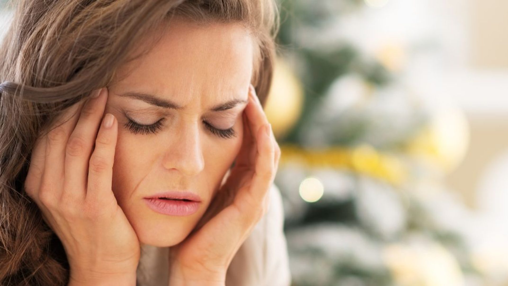 Someone with a headache from stress sitting in front of their Christmas tree.