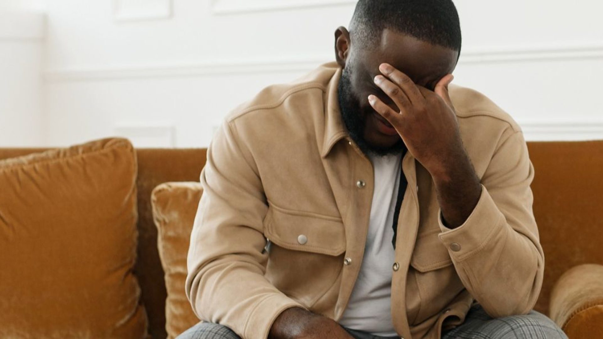 Person sitting on couch, holding hand to forehead, dealing with the symptoms of anxiety.
