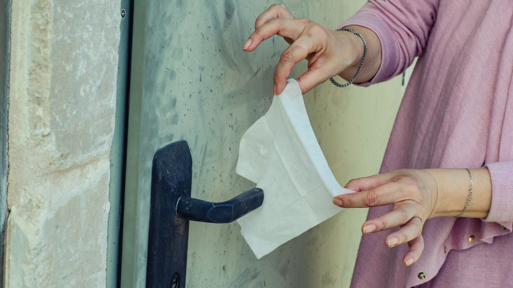 A close up photograph of a woman covering a door handle with a tissue