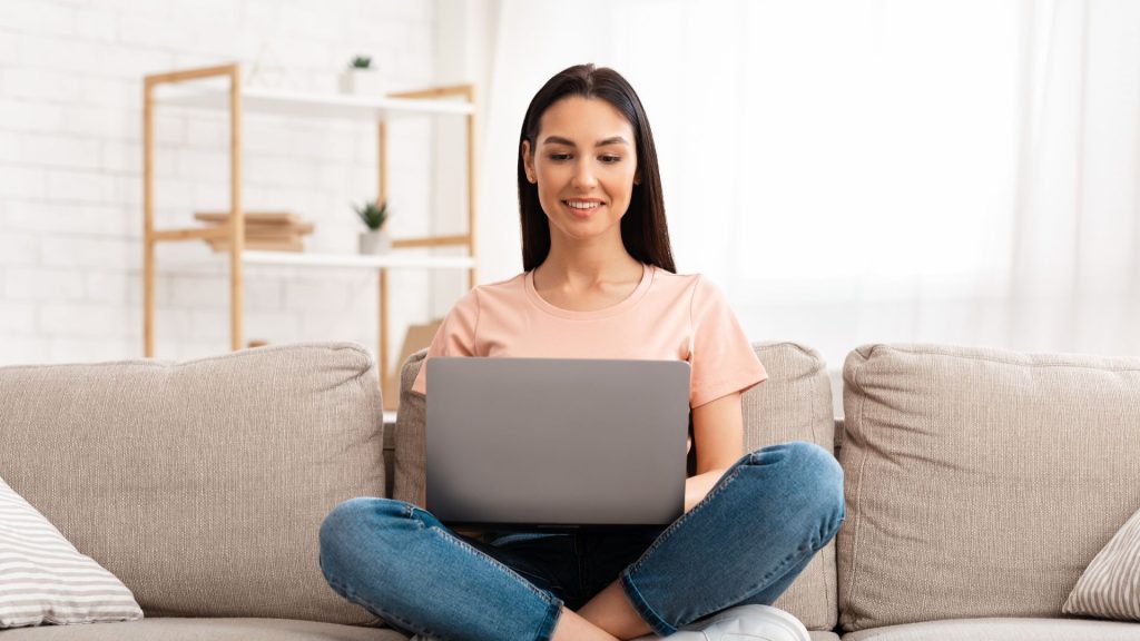 A woman on a couch attends a counseling session on her laptop