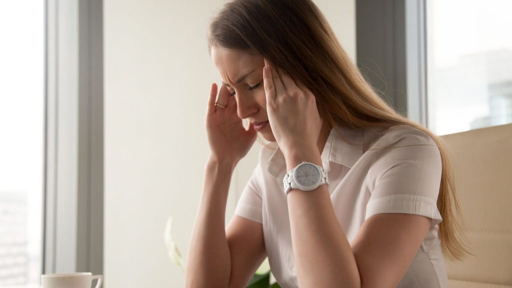 A woman who looks overwhelmed closes her eyes with her fingers against her temples