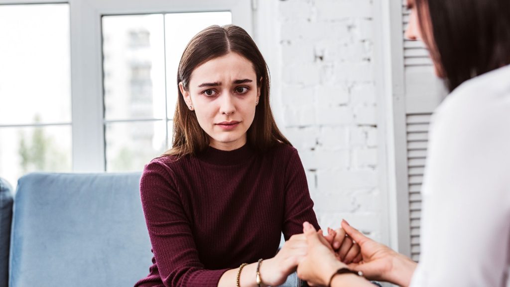 A visibly uncomfortable woman looks off into the distance while another holds her hands in support