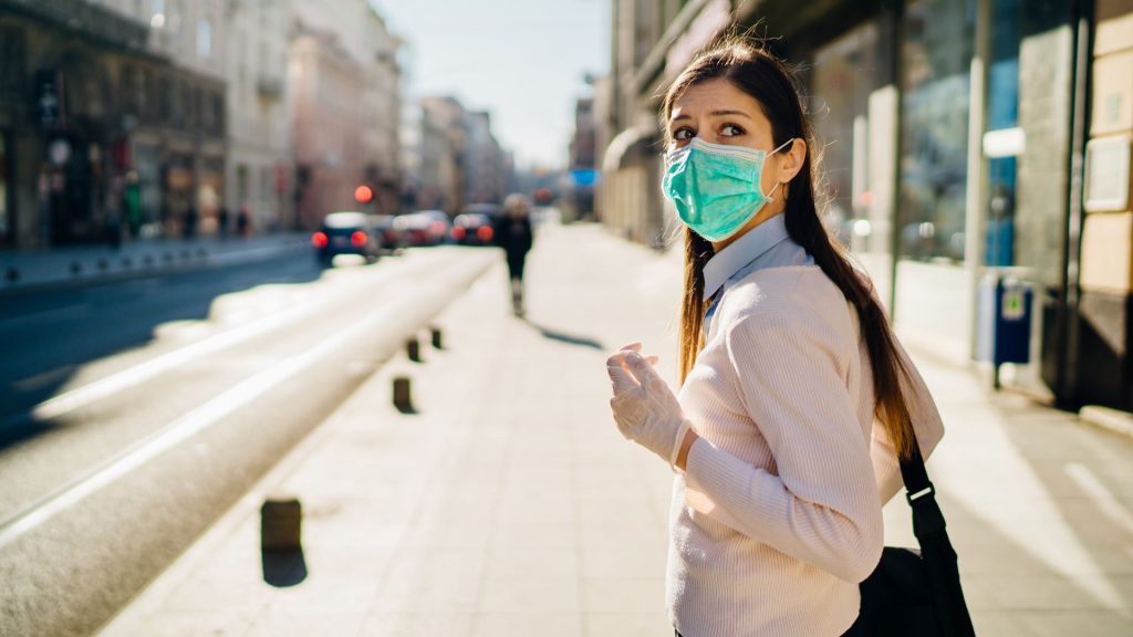 A woman with a mask and rubber gloves in public looks over her shoulder