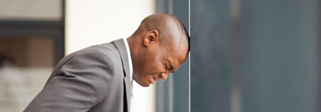 A businessperson hitting their head against the wall in frustration.