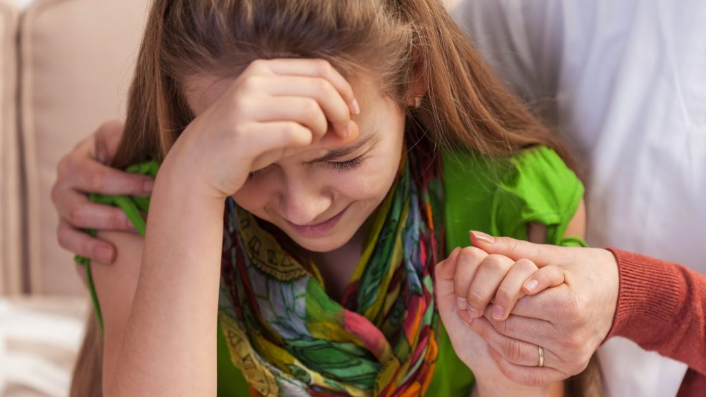 A young woman in emotional distress is comforted by another person