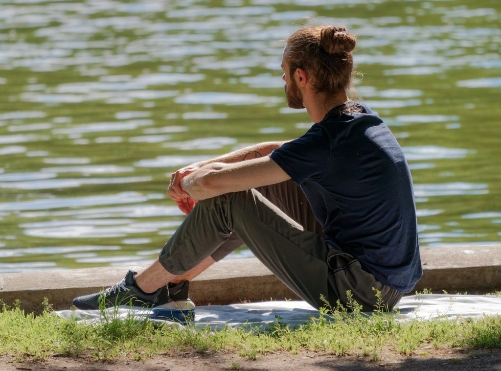 A man with arms on his knees looks out contentedly over a body of water