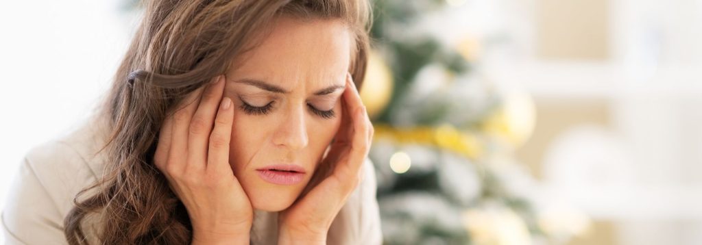 Someone with a headache from stress sitting in front of their Christmas tree.