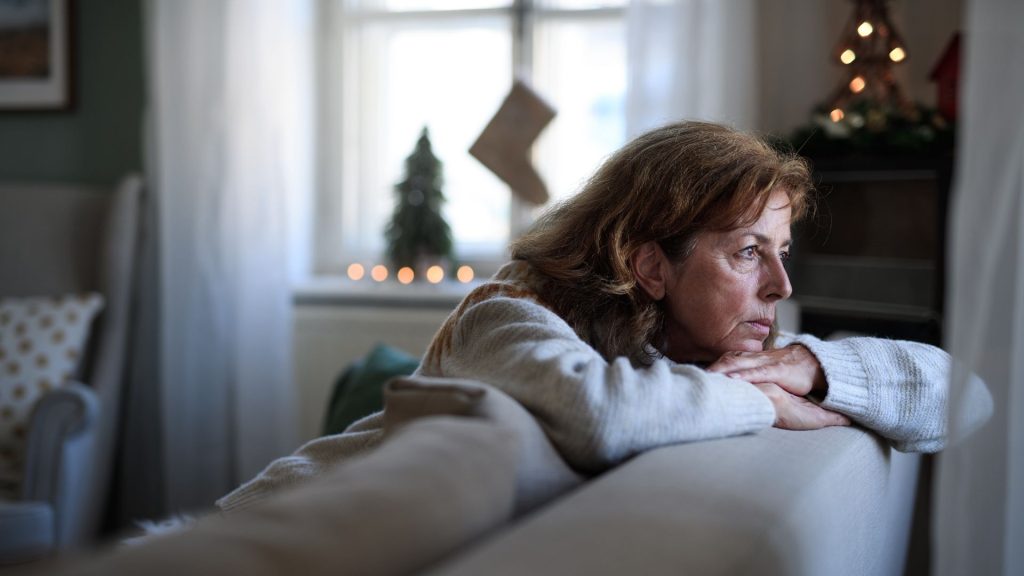 A woman looks off in loneliness in an otherwise empty room with Christmas decorations